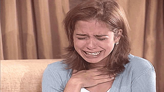 a woman in a blue sweater is crying with her hands on her chest