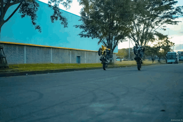two motorcycles are doing stunts on the street and the photo was taken by eddymer