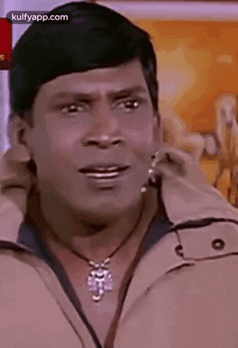 a man is wearing a necklace and a jacket and making a funny face .