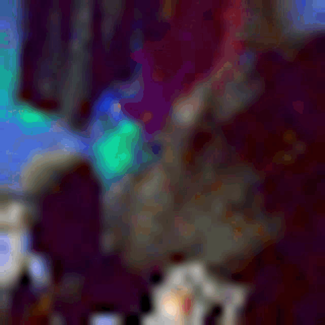 a blurry picture of a person sitting on a bed with a purple blanket and a green light behind them .