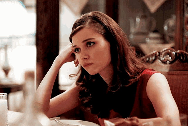 a woman is sitting at a table with her hand on her head