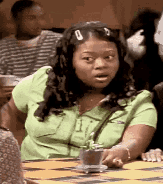 a woman in a green shirt is sitting at a table with a plate of food .