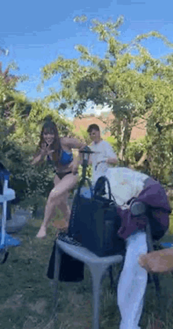 a woman in a bikini is jumping in the air while a man sits on a chair .