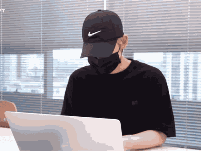 a man wearing a mask and a nike hat is using a laptop computer