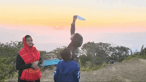 a woman and a boy are standing on top of a hill looking at the sun .