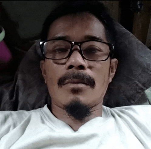 a man with glasses and a beard is laying on a bed