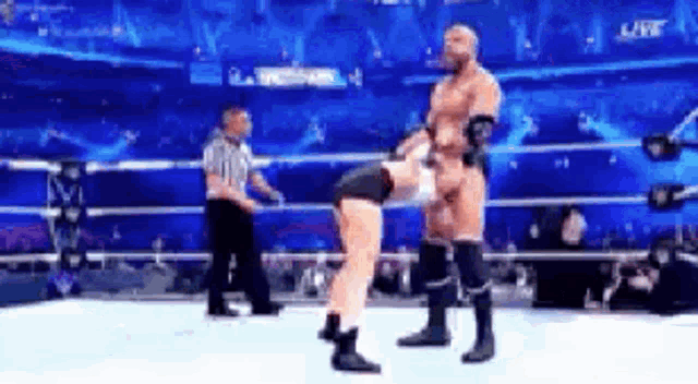 a wrestler is doing a handstand in a wrestling ring while a referee looks on .
