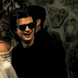 a man wearing sunglasses is standing next to a woman and smiling .