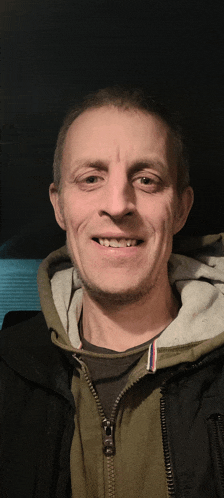 a man wearing a black jacket and a green hoodie smiles