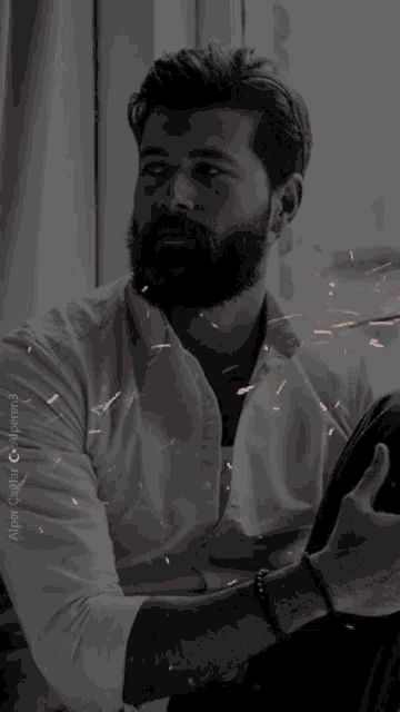 a man with a beard wearing a white shirt is sitting in front of a window in a black and white photo