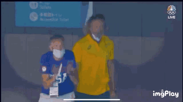 a man wearing a mask is standing next to another man wearing a yellow shirt .
