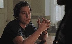 a young man is sitting at a table with his hands folded in prayer .