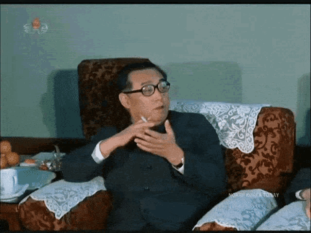 a man is sitting in a chair smoking a cigarette with the words north korea today on the bottom right
