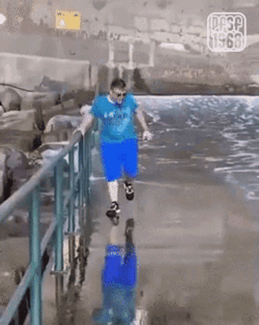 a man in a blue shirt and blue shorts is jumping over a railing