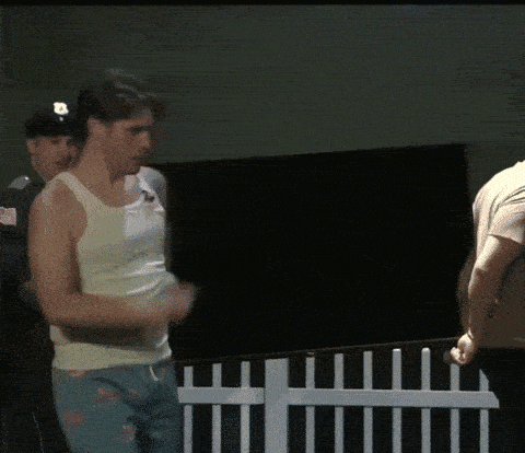a man in a white tank top stands in front of a fence
