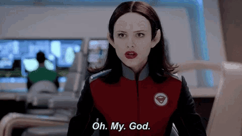 a woman in a red jacket is standing in a room and saying `` oh , my god '' .