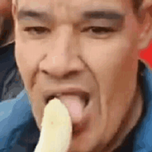 a close up of a man eating a banana with his tongue sticking out .
