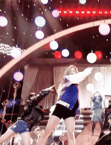 a woman in a blue jacket and black shorts is dancing on stage