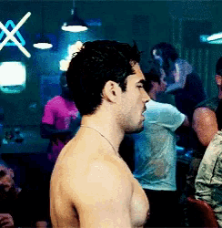 a shirtless man is standing in a crowded room with a neon sign that says x