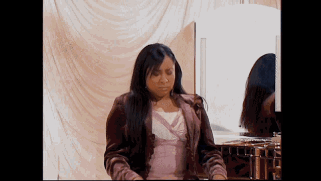 a woman in a pink jacket is looking at herself in a mirror
