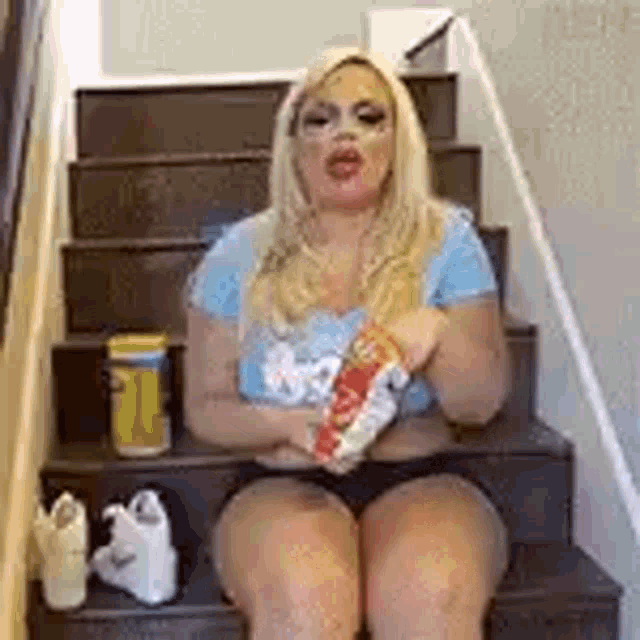 a woman is sitting on a set of stairs holding a can of soda and a bag of chips .