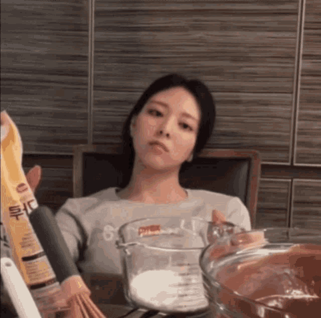 a woman is sitting at a table holding a measuring cup and a bag of flour .