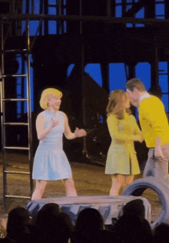 a man in a yellow sweater shakes hands with two women