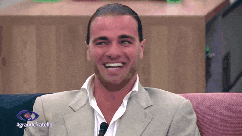 a man in a suit is smiling in front of a large eye with the hashtag grandefratello