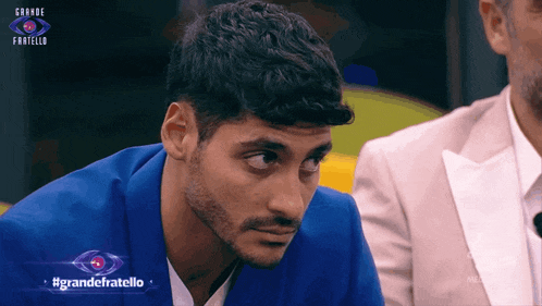 a man in a blue suit is sitting in front of a sign that says grande fratello on it