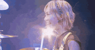 a woman is playing drums on a stage with a purple background