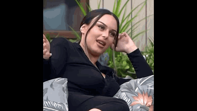 a woman in a black dress is sitting in a chair with a pillow and talking on a cell phone .