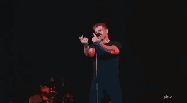 a man is singing into a microphone on a stage while making a middle finger gesture .