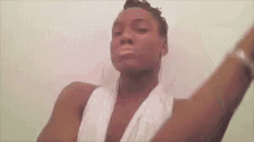 a woman is standing in front of a white wall with her arms outstretched and a towel around her neck .