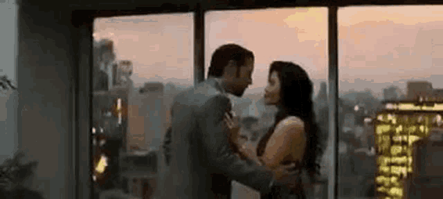 a man and woman are kissing in front of a window .
