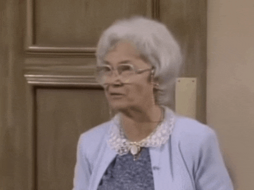 an elderly woman wearing glasses is holding a piece of cheese in her hand .