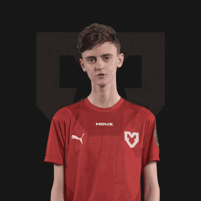 a young man wearing a red mouz shirt stands in front of a dark background