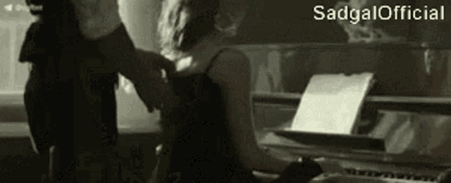 a woman in a black dress is playing a piano while a man stands behind her ..