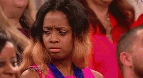 a woman in a pink dress is making a funny face while sitting in a crowd of people .