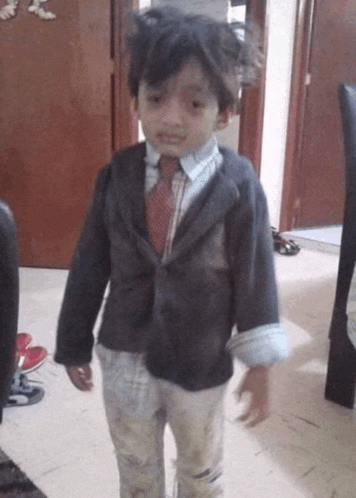 a young boy wearing a suit and tie standing in a hallway