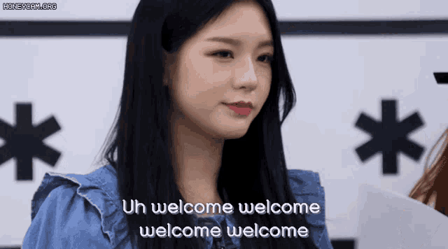 a woman with long black hair is standing in front of a sign that says uh welcome welcome welcome welcome