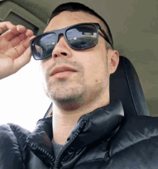 a man wearing sunglasses and a black jacket looks at the camera