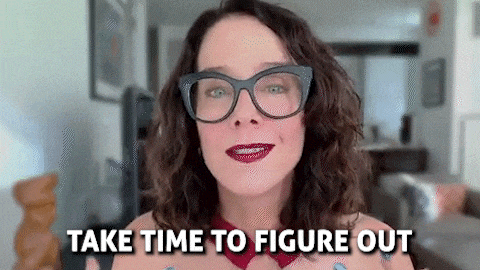 a woman wearing glasses and red lipstick is standing in a living room and says `` take time to figure out '' .
