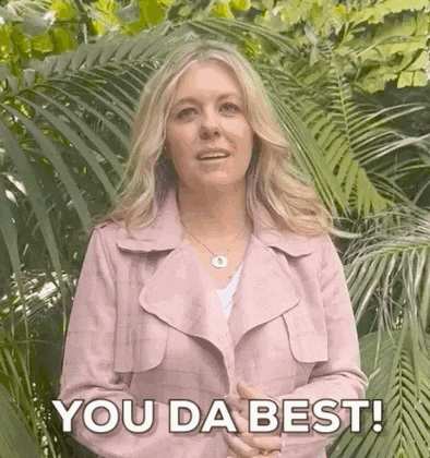 a woman in a pink jacket is standing in front of a palm tree and says `` you da best '' .