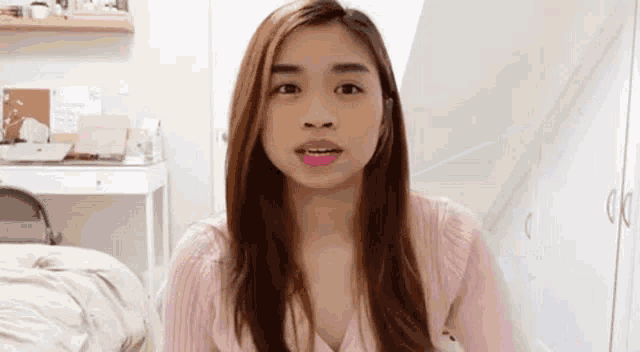 a woman in a pink sweater is sitting in front of a bed in a room .