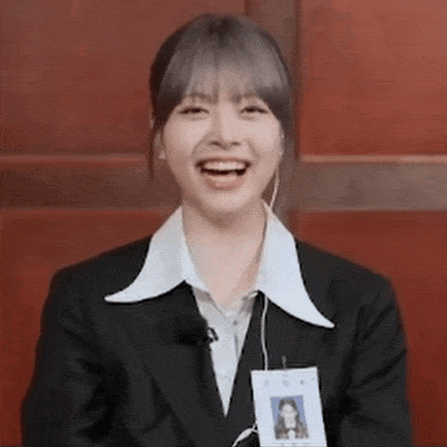 a woman in a suit and white shirt is smiling while wearing a name tag .