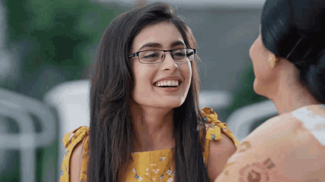 a woman wearing glasses and a yellow dress smiles at another woman