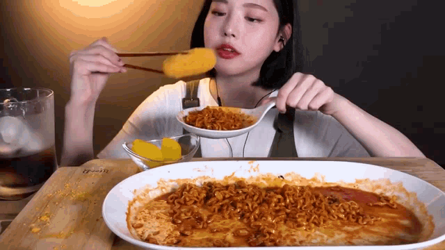 a woman is eating noodles with chopsticks and a bowl of pickles