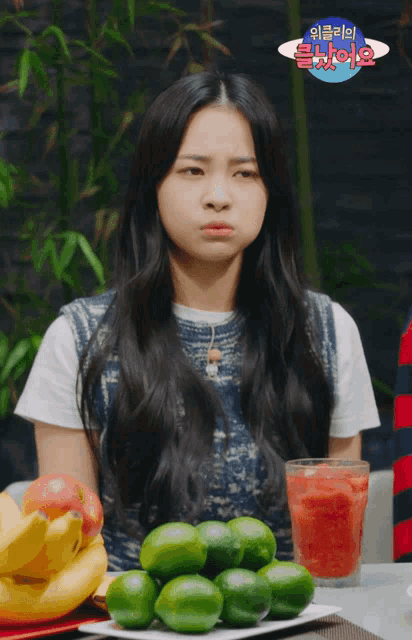 a woman is sitting at a table with a plate of limes and a glass of watermelon juice