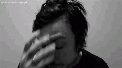 a man is covering his face with his hands while smoking a cigarette .