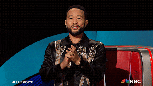 a man sitting in a chair with his arms outstretched and a nbc logo behind him